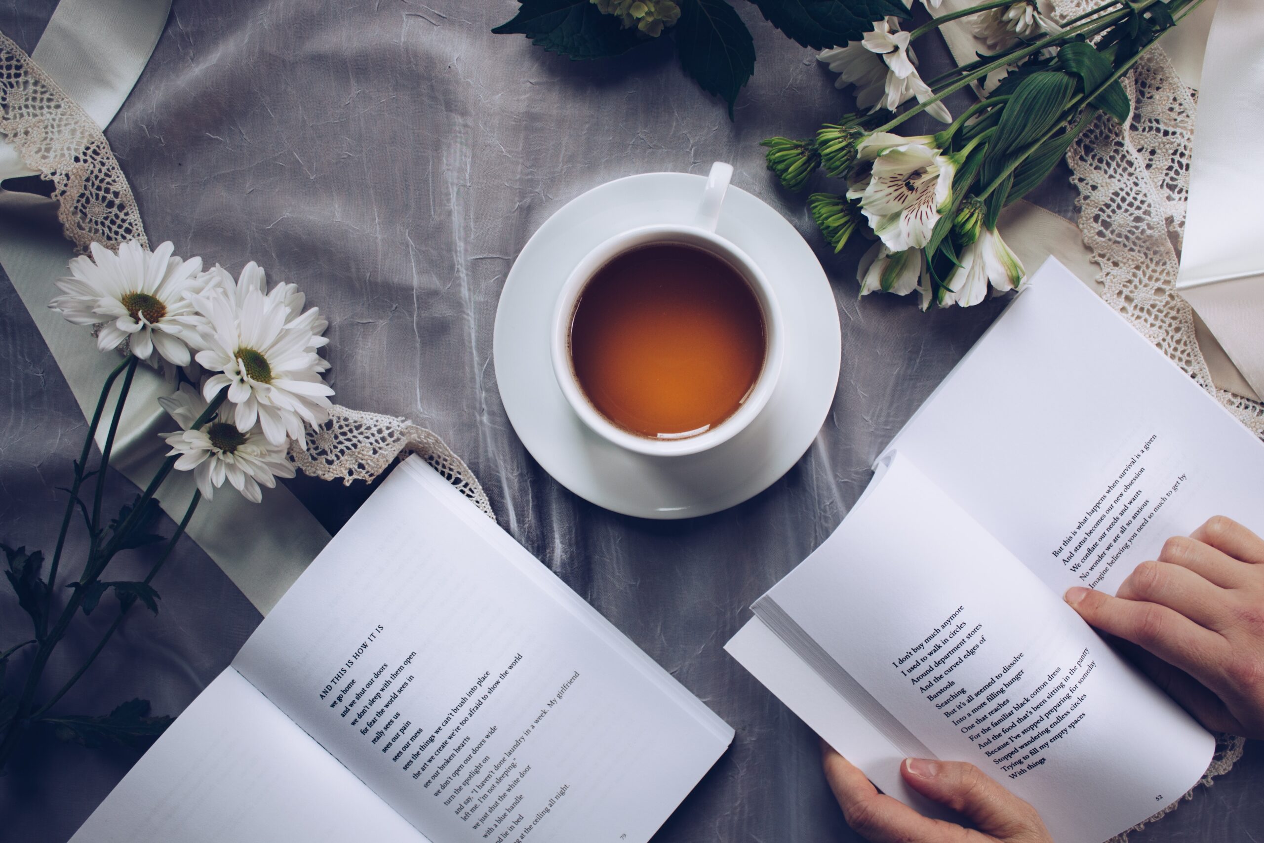 Photograph of two open poetry books, a small cup of tea, and white flowers